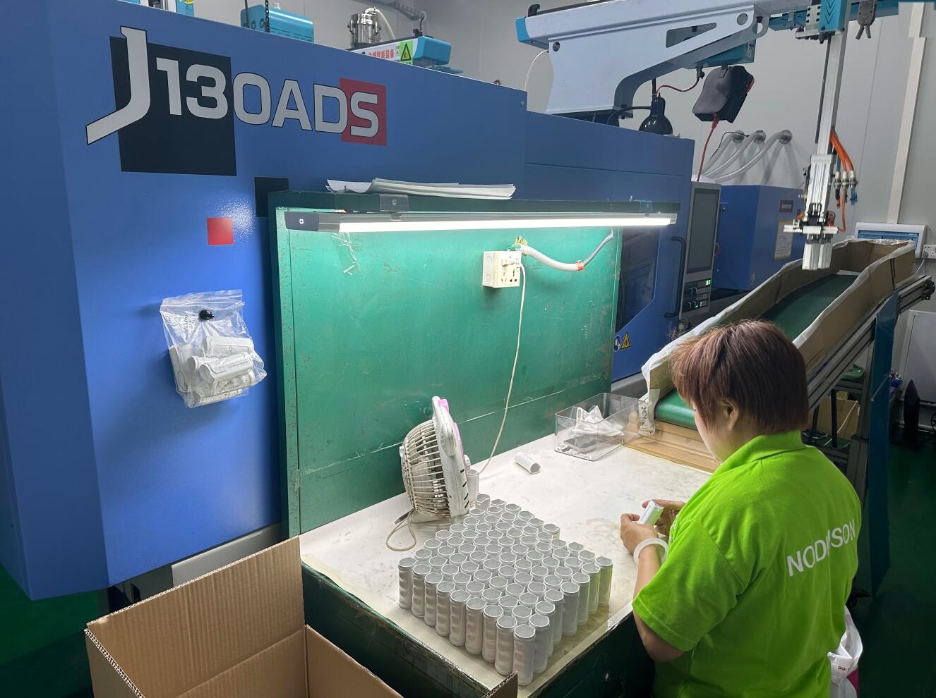 Woman in a green NODINSON polo shirt at an injection molding workstation